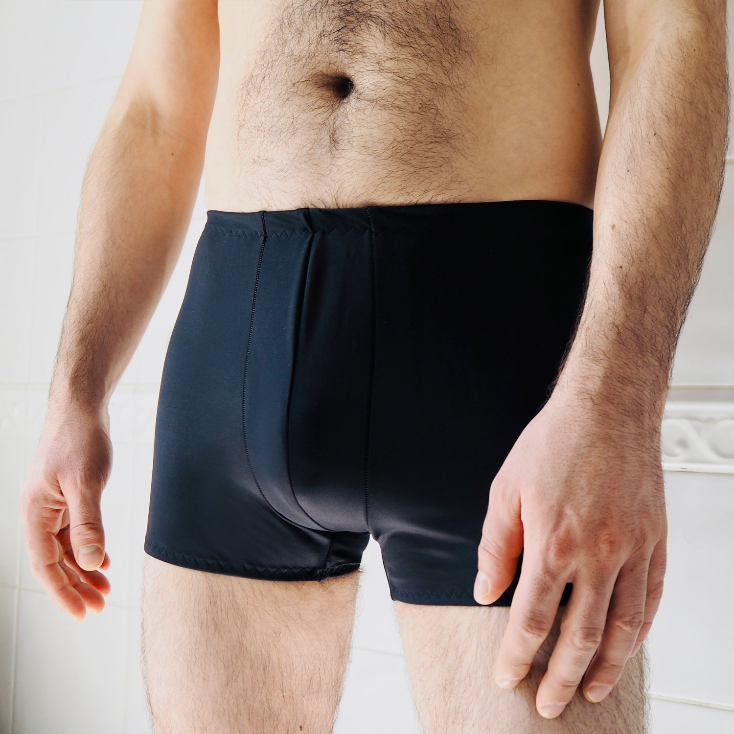 Lower body of a man with a hairy body wearing black tight trunks